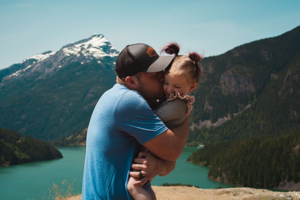 A father carrying a daughter and standing by a mountainside